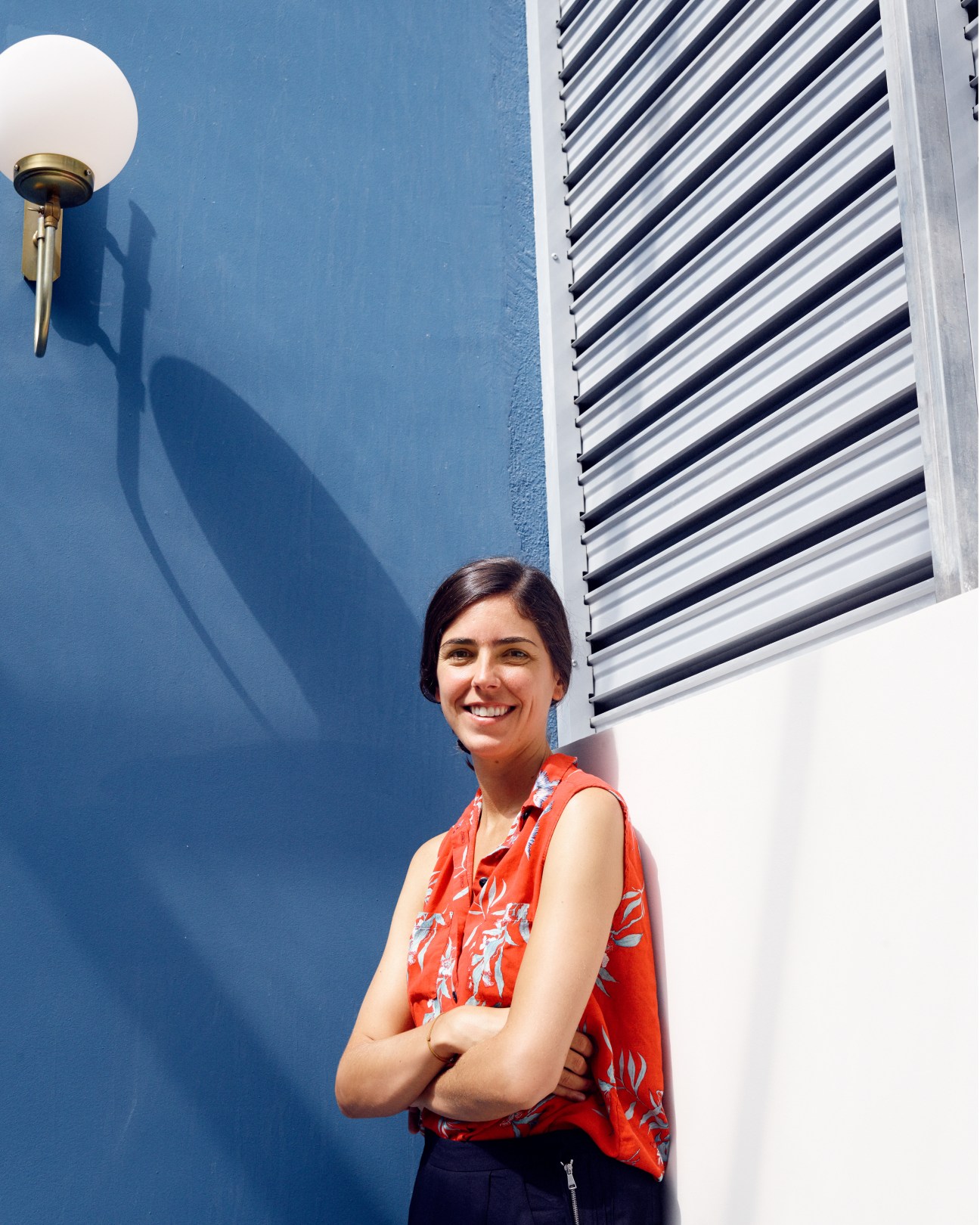 Ines Miró Sans, founder of Casa Bonay hotel, smiling against a bright blue wall with a round wall sconce above her.