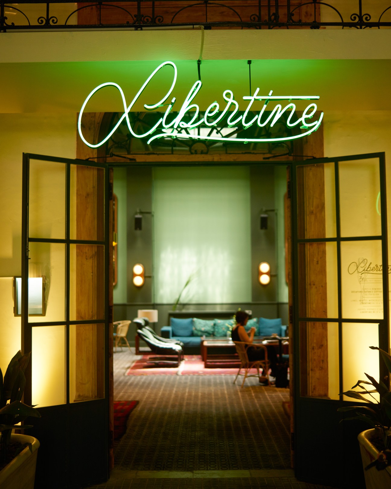 Casa Bonay hotel entrance with neon 'Libertine' sign above wooden doors opening to illuminated lounge interior.