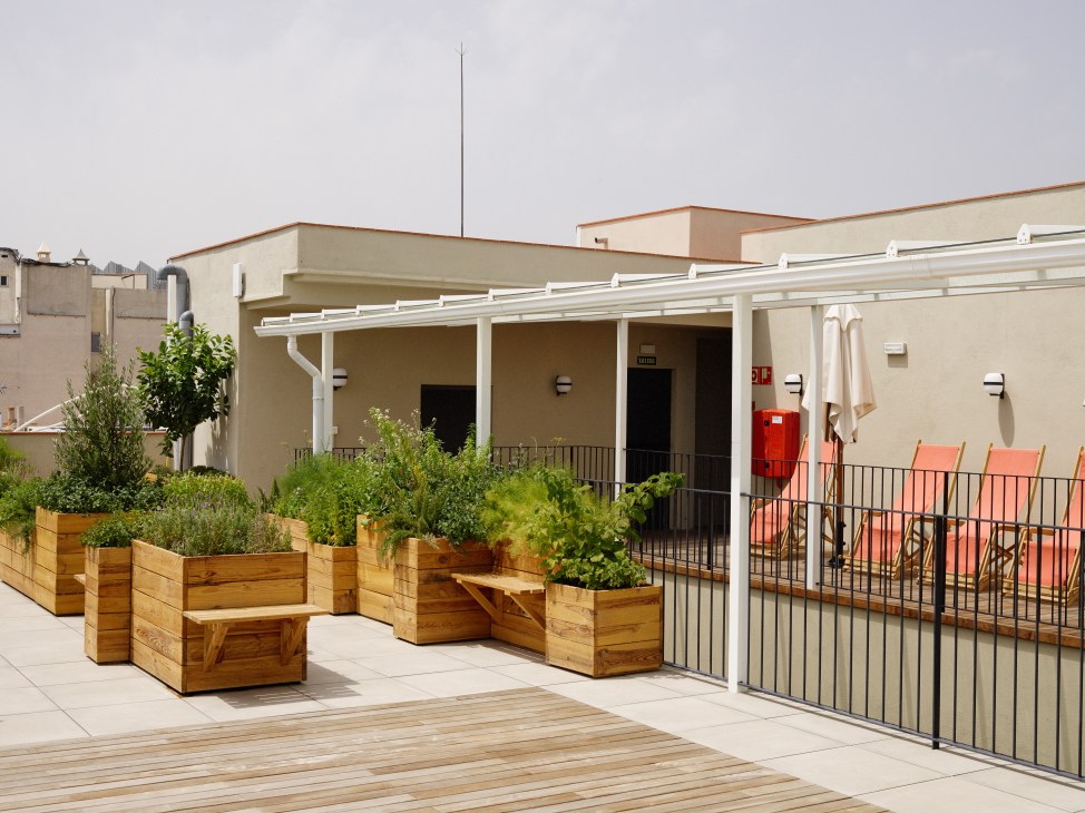 Casa Bonay rooftop terrace with wooden planters, white pergola, orange chairs, and beige building facade.