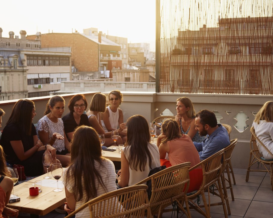 Guests and locals gather on Casa Bonay rooftop at sunset with Barcelona cityscape in background.