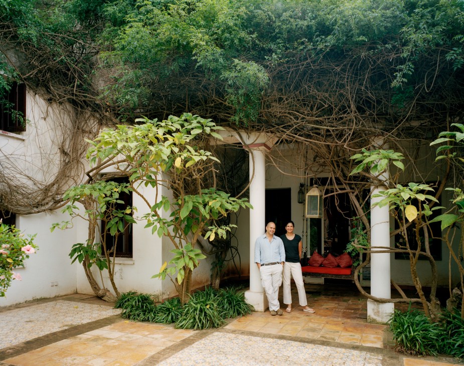 Tahir and Rachana Shah stand in the courtyard of their Casablanca home, surrounded by overgrown vines and plants.