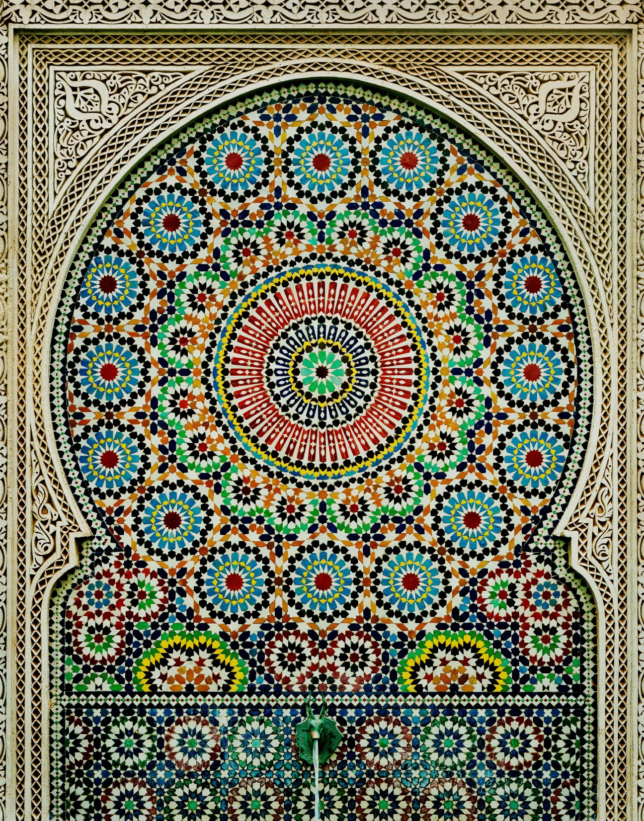 Intricate geometric mosaic tilework with concentric circles of turquoise, red, green and gold patterns surrounding a central medallion.