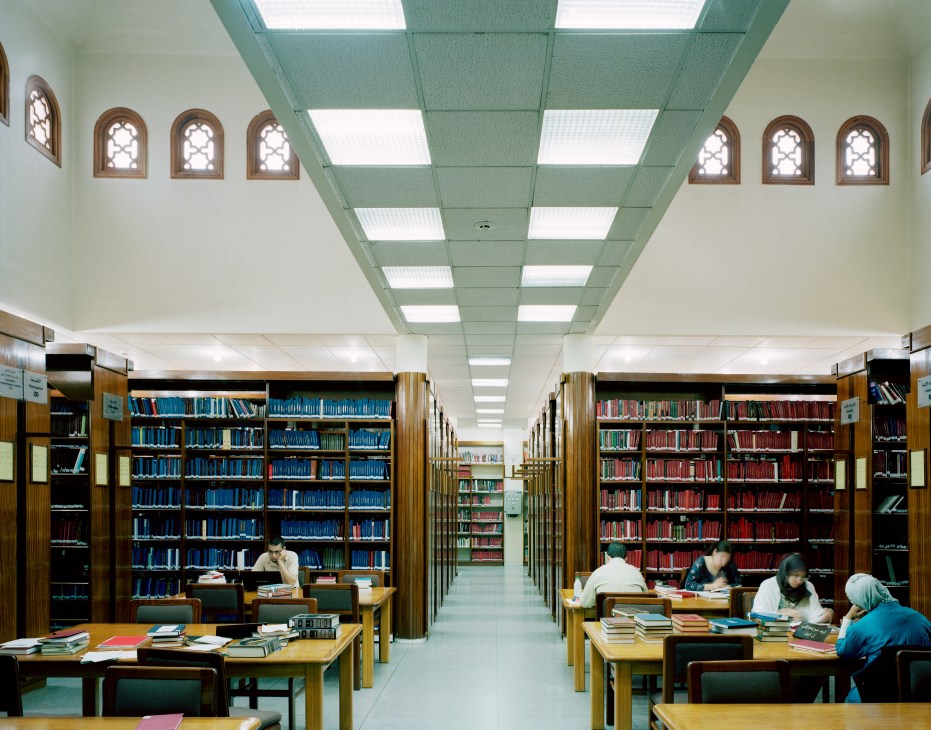 Interior of Bibliothèque Al Saoud library with wooden bookshelves, reading tables, and geometric patterned windows.