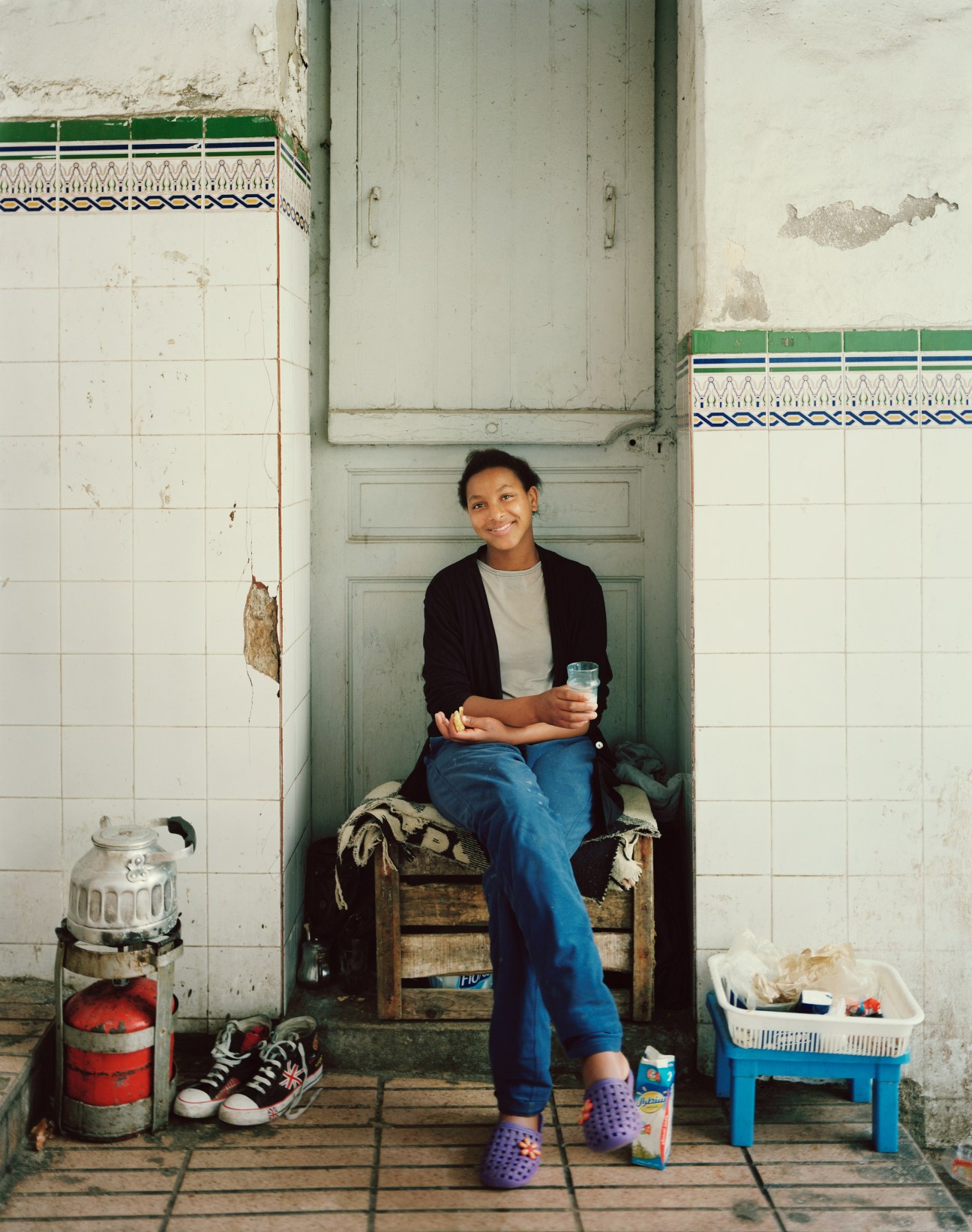 Young woman sitting in a doorway at Le Marché Central market in Casablanca, holding a glass of water.