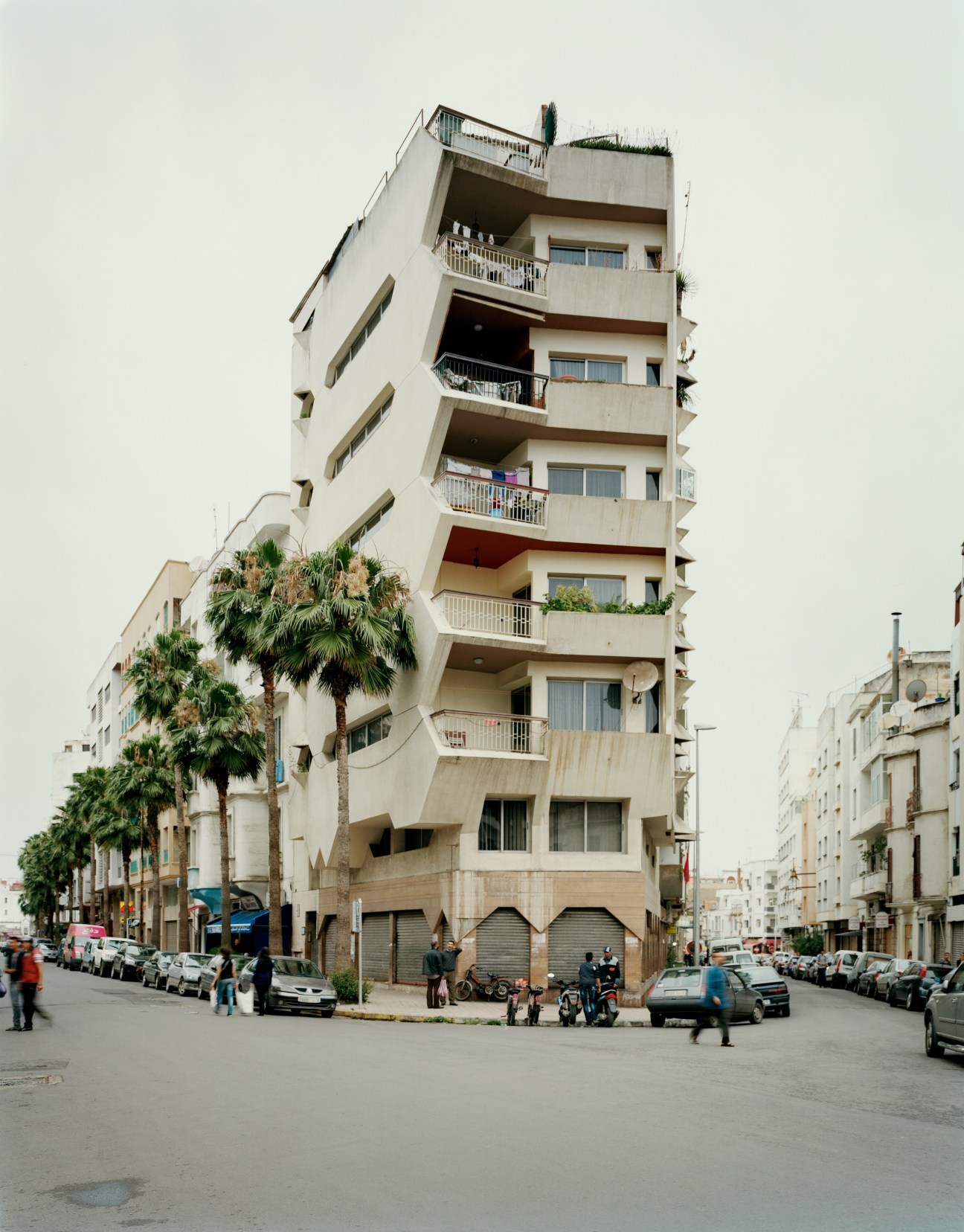 Multi-story apartment building with palm trees and parked cars on a Casablanca street.