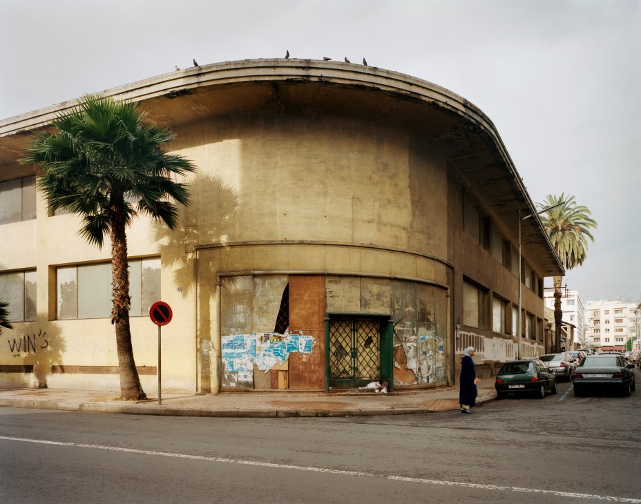 Curved Art Deco building with weathered cream-colored facade, palm trees, and boarded-up windows on Avenue Mers Sultan, Casablanca.