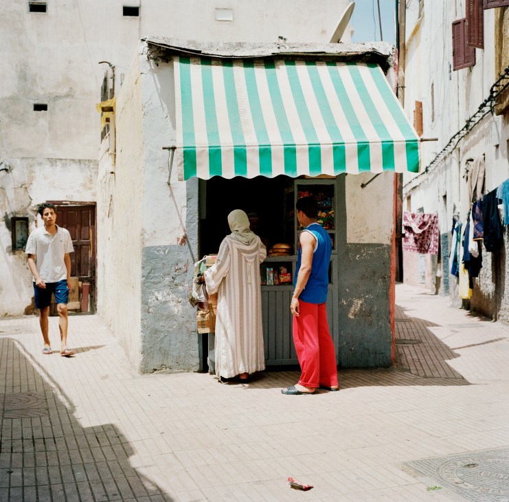 Shop in the Old Medina with green and white striped awning, weathered white buildings, and people in traditional dress.