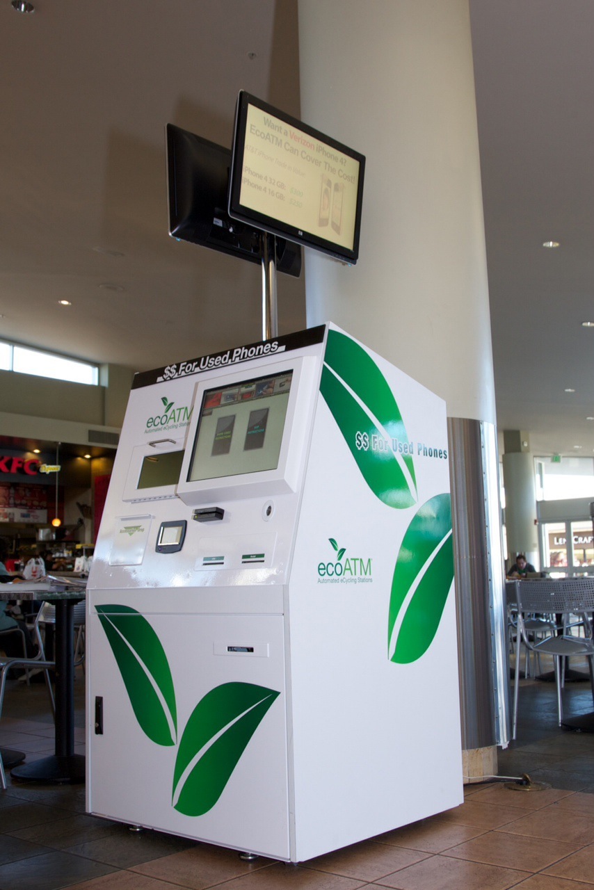 ecoATM kiosk with white and green design for recycling used mobile phones in a shopping mall.