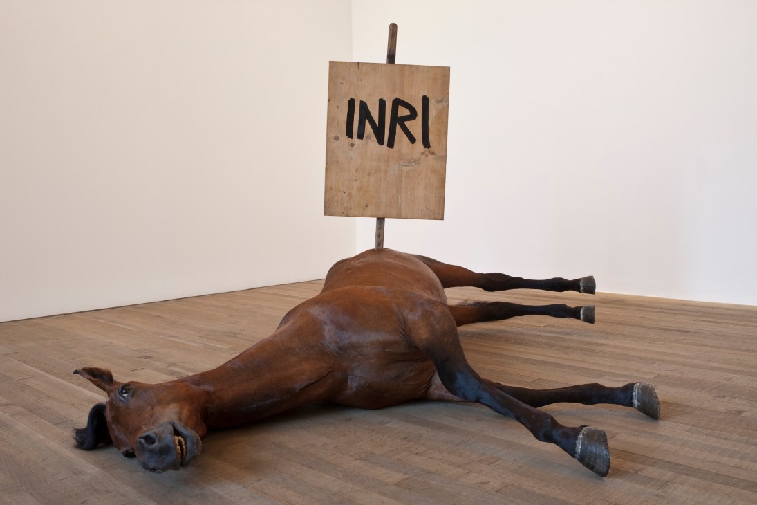 Maurizio Cattelan's sculpture of a prone horse with a wooden sign reading 'INRI' mounted on a pole above it.