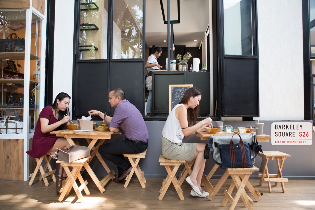 Diners eating at wooden tables outside Corner de Bark noodle restaurant at The Barkyard Bangkok.