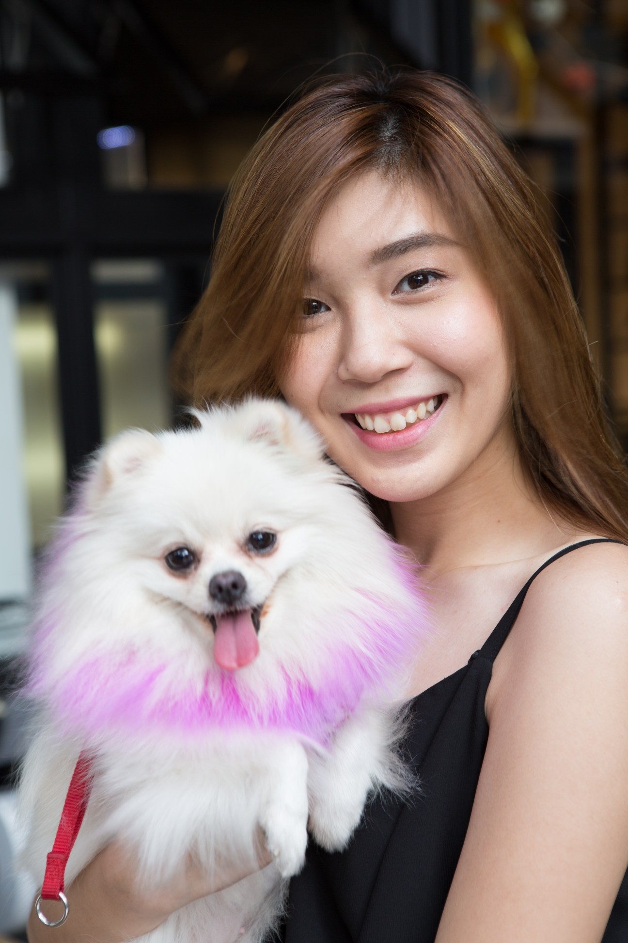 Dear Pitaksantayothin smiles while holding her white Pomeranian dog, Money, with pink dyed fur.