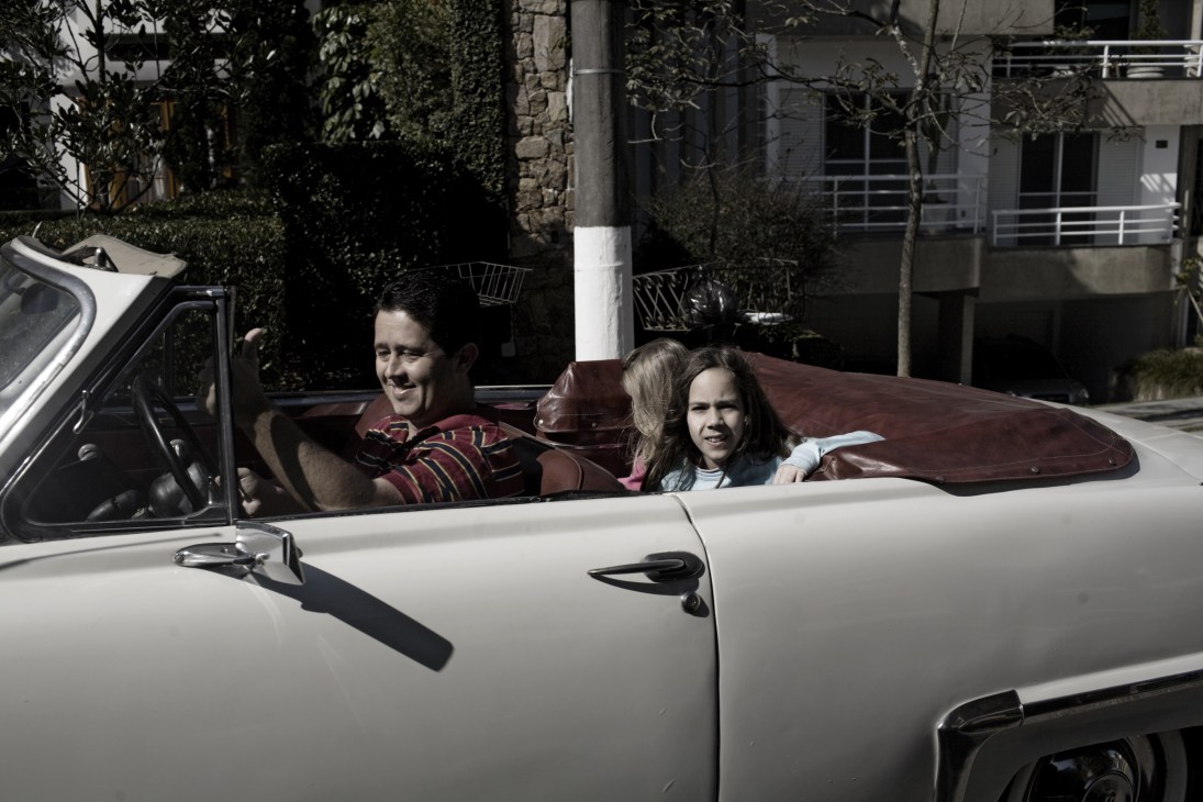 A father and child ride in a 1950s Plymouth convertible with the top down in AlphaVille.