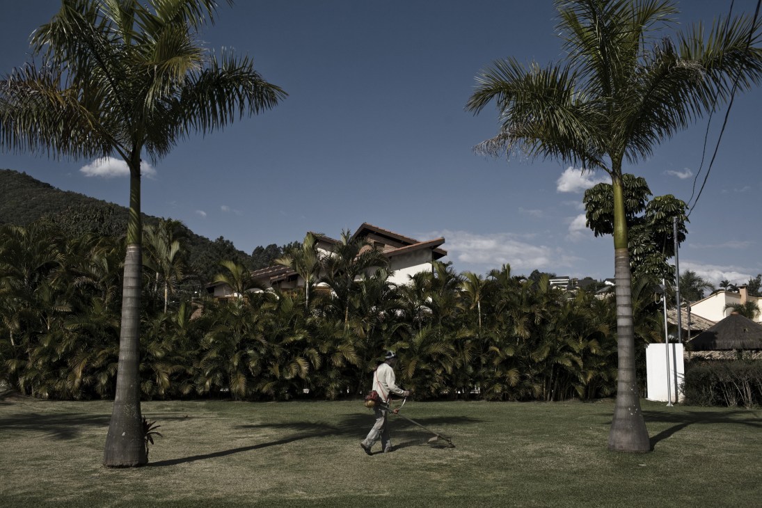 A gardener walks across a manicured lawn lined with palm trees in AlphaVille gated community.
