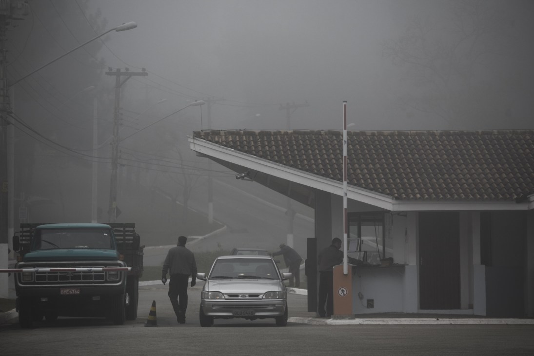 Security personnel stop vehicles at a gated community entrance gate in heavy fog.