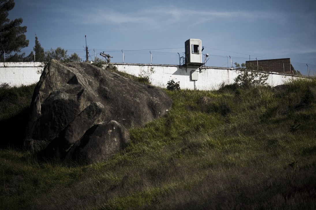 A security guard tower mounted on a white wall overlooking grassland in a gated community.