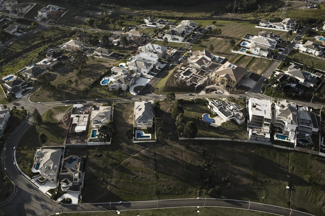 Aerial view of Tambore 2 gated community showing rows of houses with swimming pools and manicured lawns separated by curved streets.