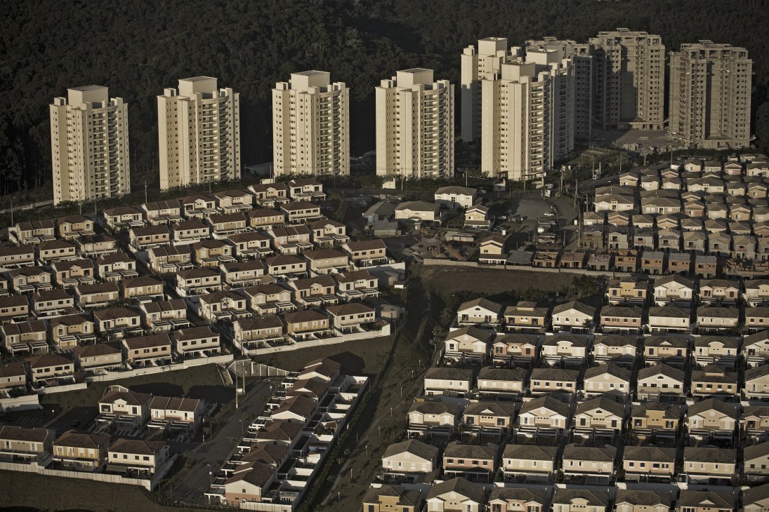 Aerial view of Tambore 2 gated community showing rows of uniform single-family homes and tall apartment buildings surrounded by forest.