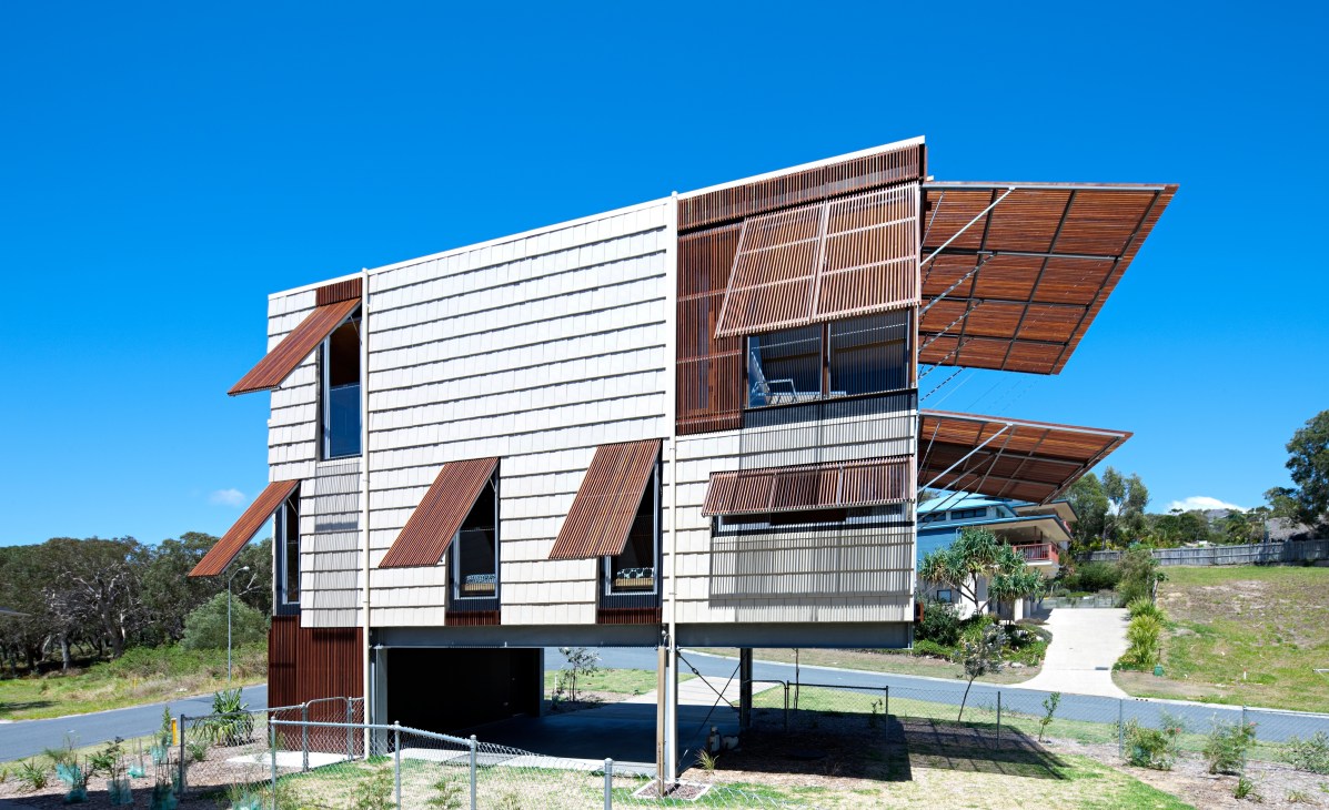 Modern beach shack with white and terracotta corrugated metal facade and wooden shutters on Stradbroke Island, Australia.