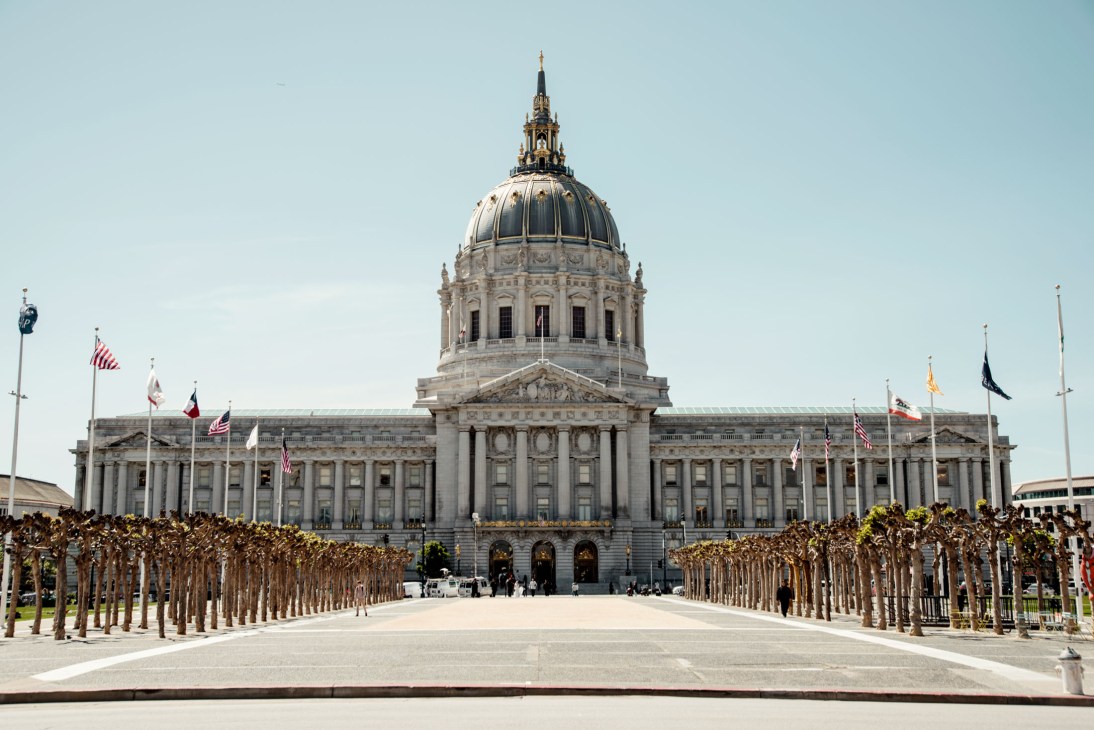 San Francisco City Hall's neoclassical facade with dome and flags under blue sky.