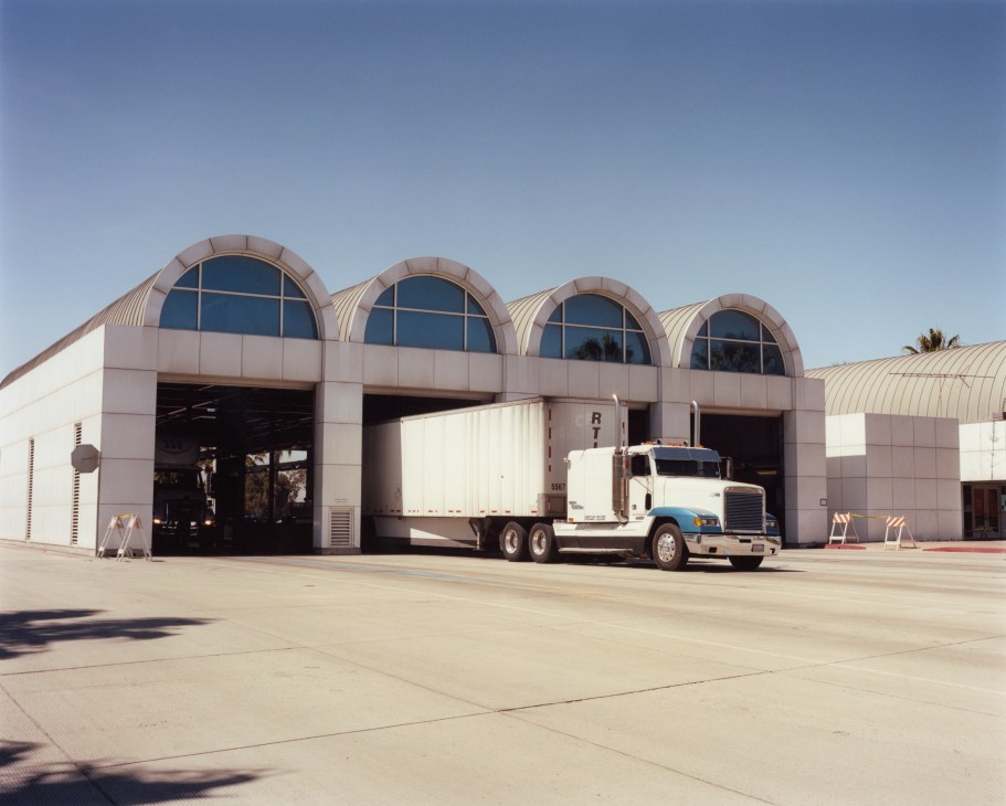 A white semi-truck parked at a modern warehouse facility with distinctive arched windows in Otay Mesa.