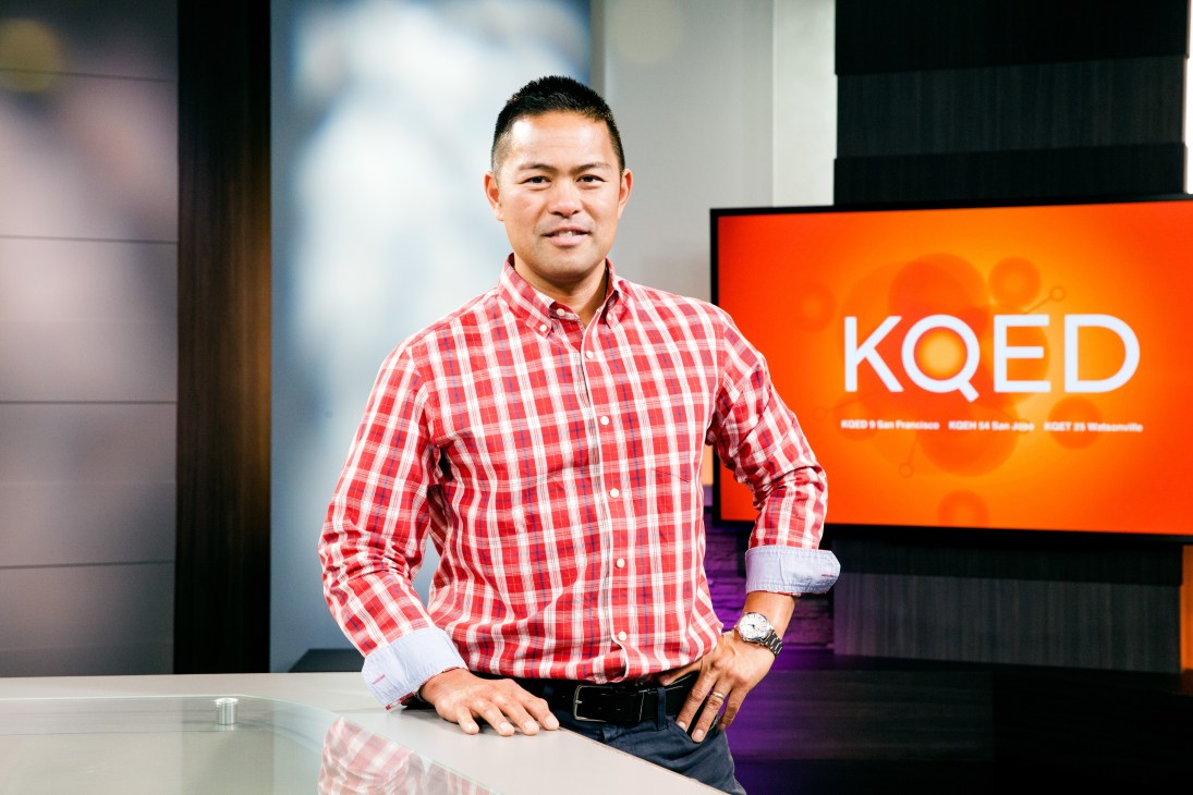 Michael Isip, senior vice-president and chief content officer at KQED, standing in front of an orange KQED branded display.