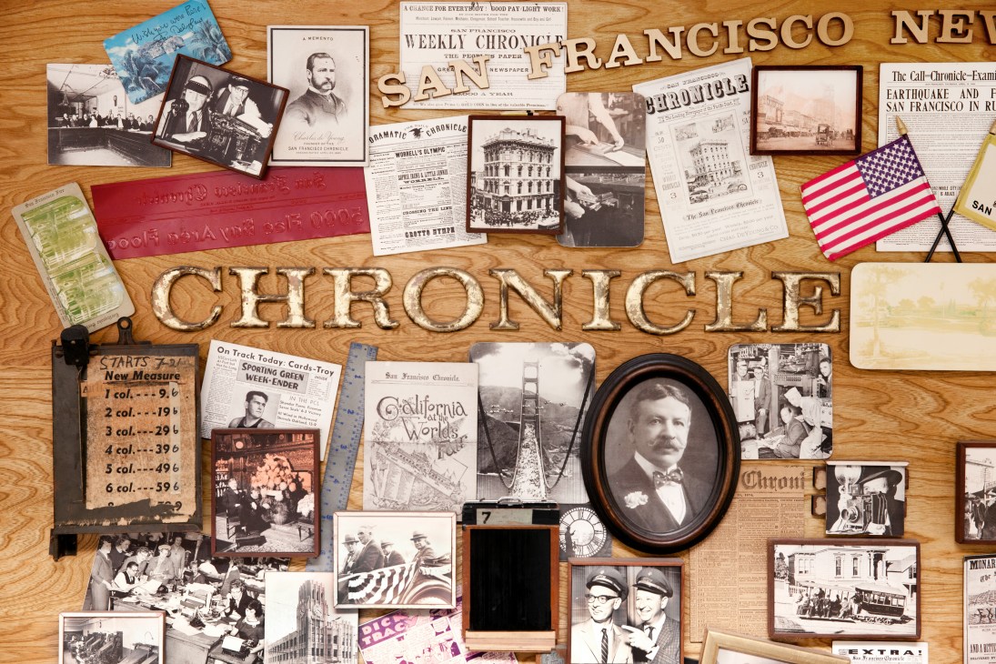 Wooden display board with San Francisco Chronicle newspaper memorabilia, vintage photographs, portraits, and historical documents arranged artfully.