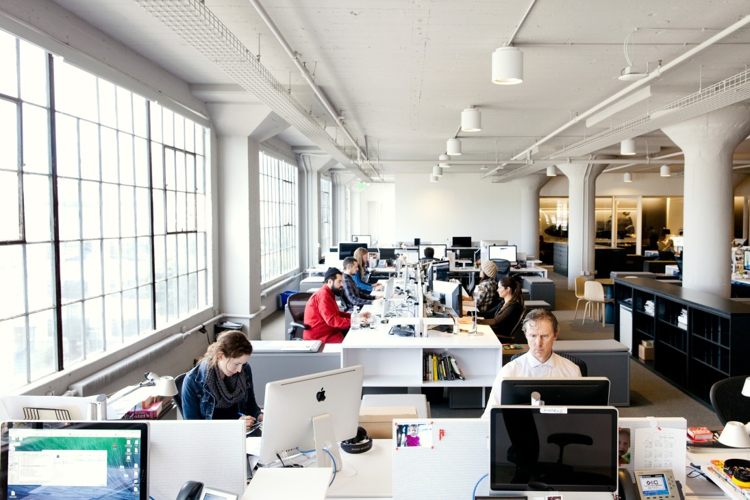 Wired magazine headquarters office with employees working at desks in a modern open-plan workspace with white columns and large windows.