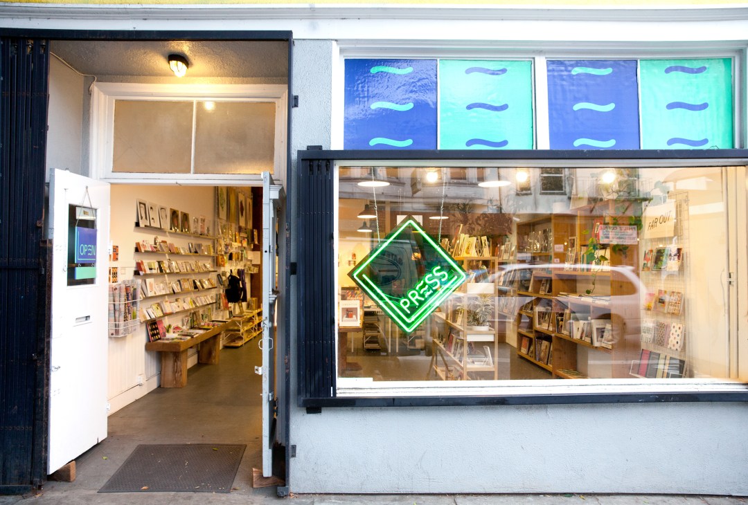 Press bookshop storefront in San Francisco's Mission District with green neon sign and display windows.