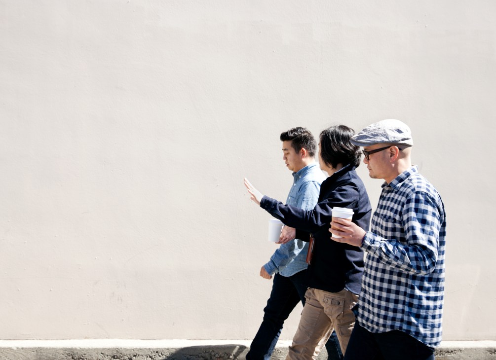 Three men walking together returning from lunch, one holding a coffee cup.