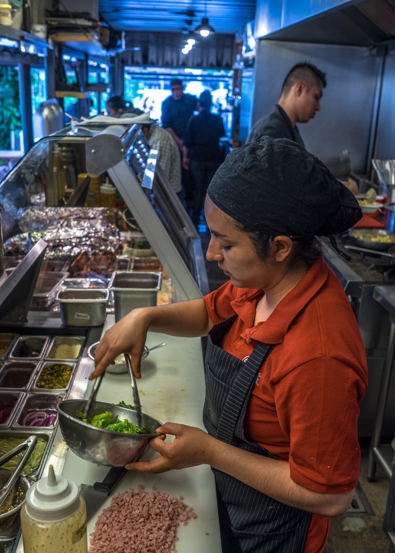 A chef in an orange shirt and black apron prepares food at Porco Rosso's kitchen counter.