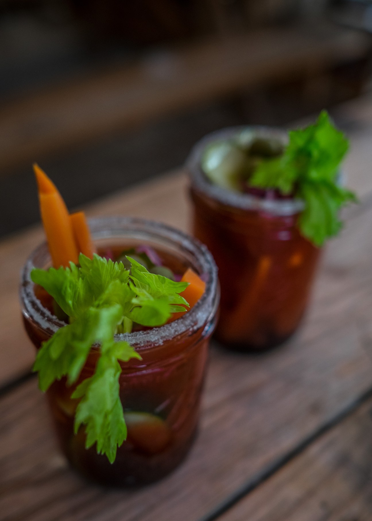 Two dark cocktails garnished with fresh cilantro and orange slices on a wooden surface.