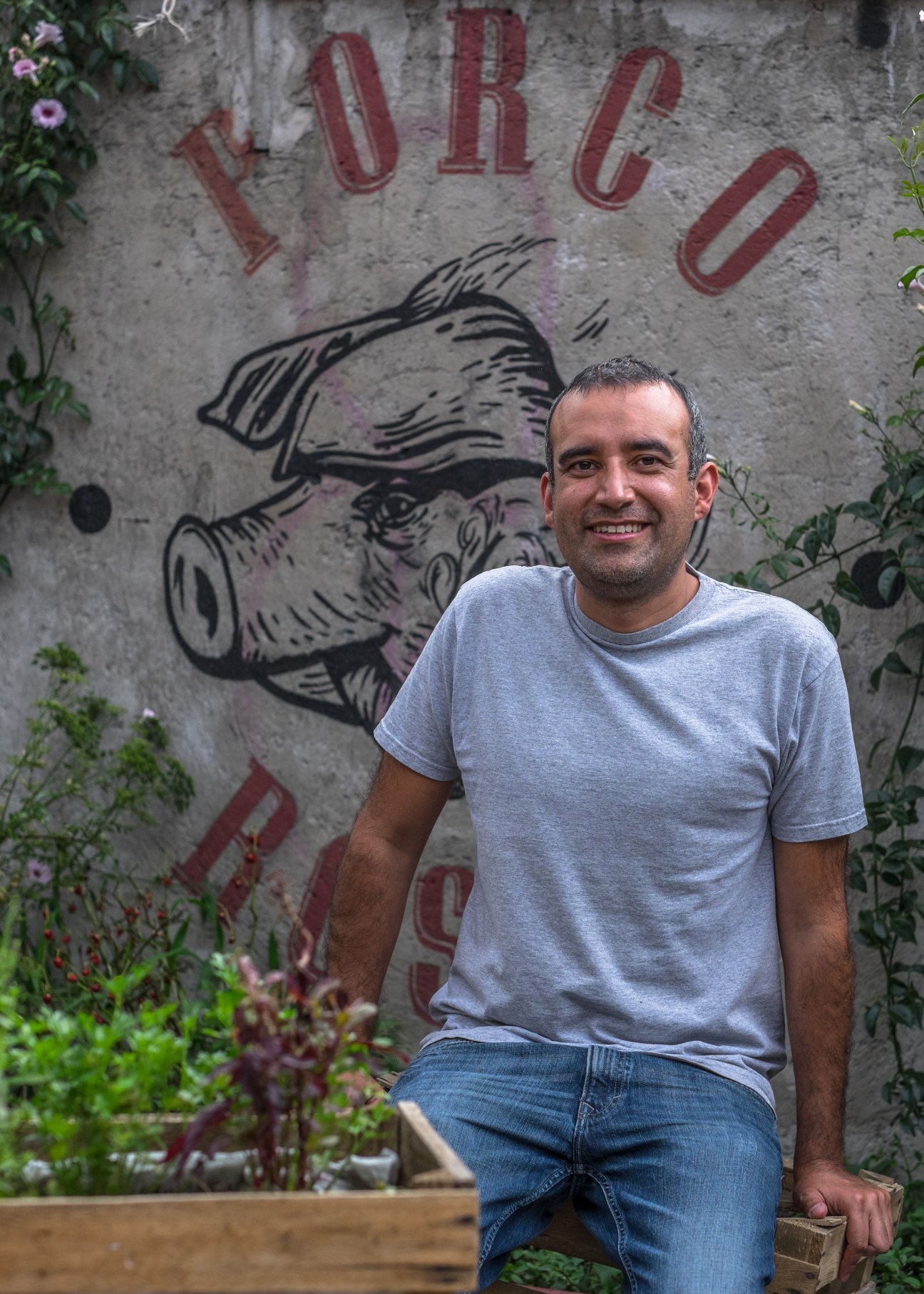 Pedro Ochoa, co-owner of Porco Rosso, standing in front of a wall with a pig illustration and restaurant signage.