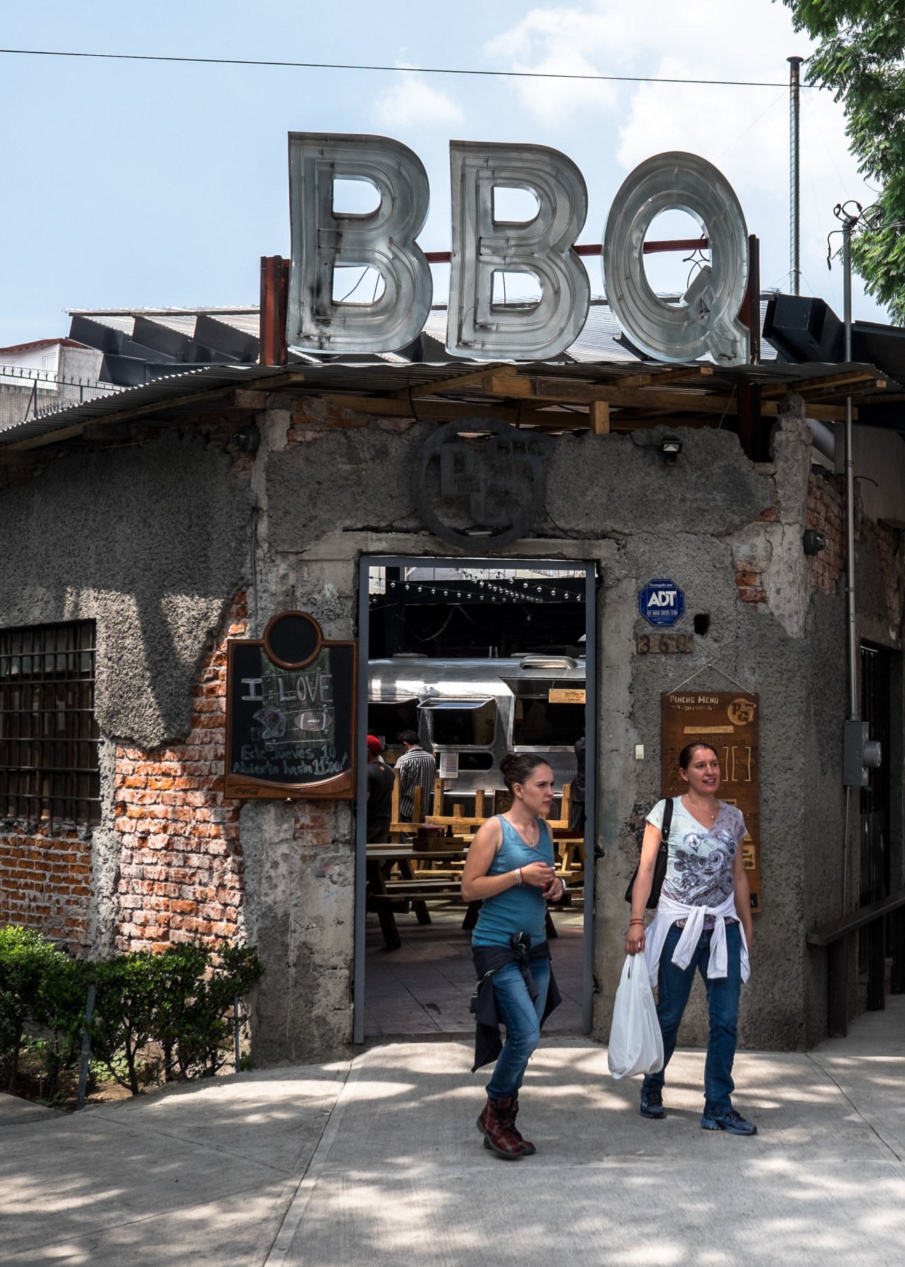 Pinche Gringo BBQ restaurant exterior with neon sign and customers walking past the entrance in Mexico City.