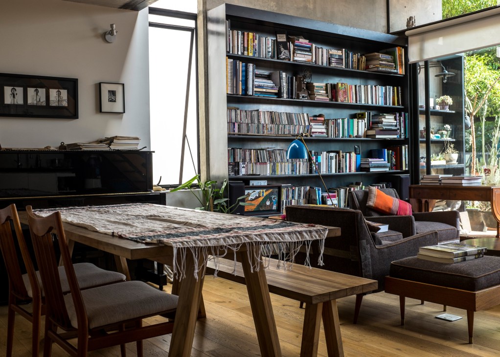 Modern loft interior with black bookshelf, dining table, and natural light from large windows.
