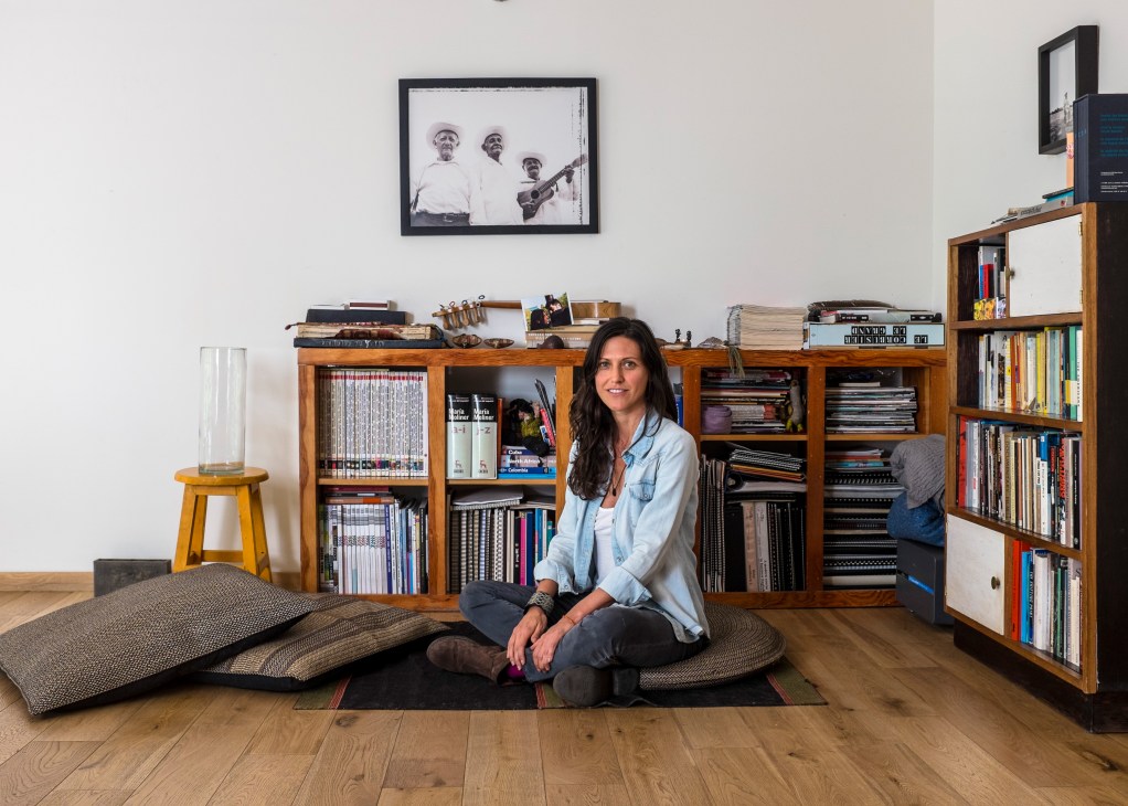 Claudia Rodriguez sits in her Mexico City loft lounge, surrounded by wooden bookshelves and artwork.