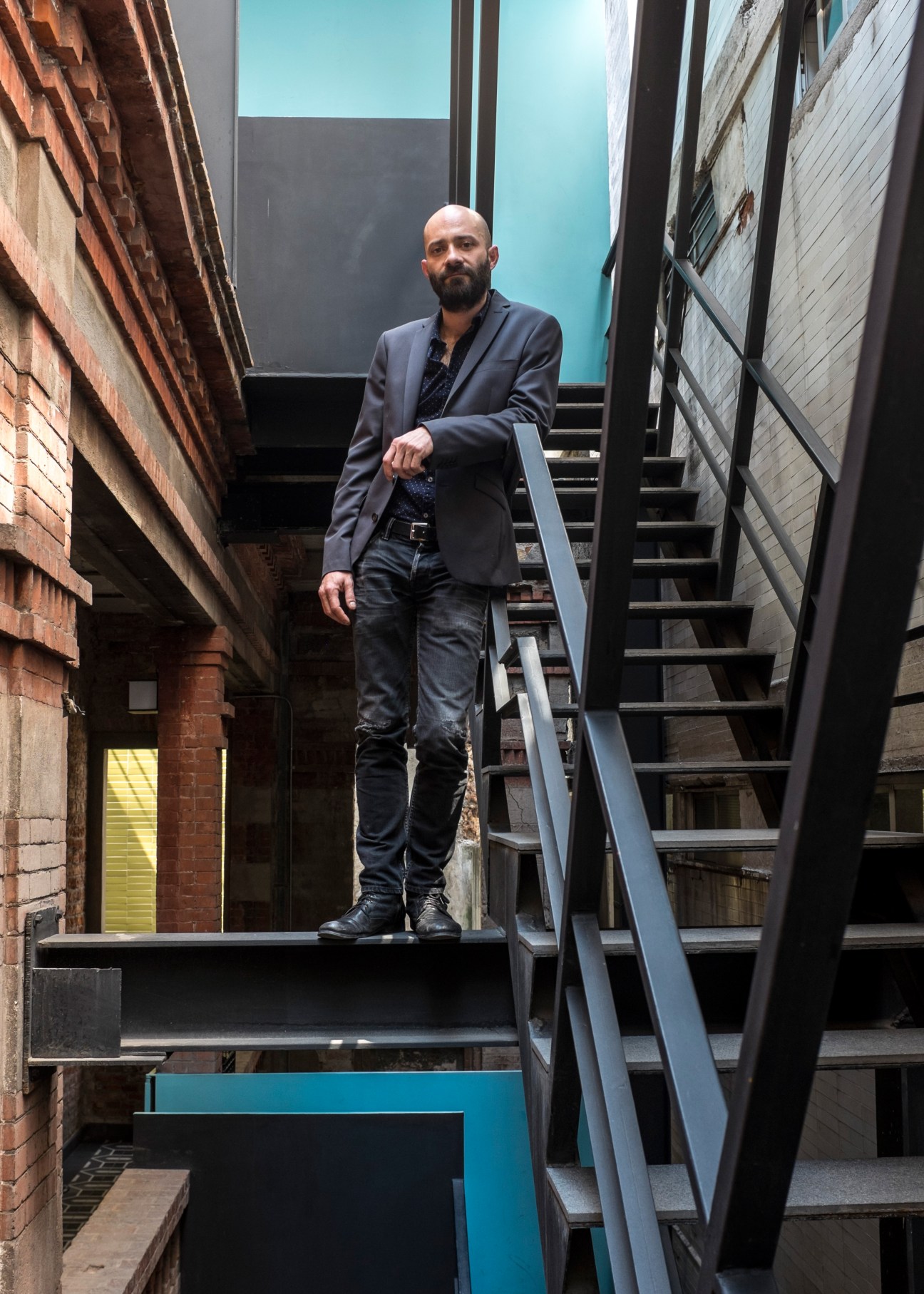 Architect Pancho Pardo stands on stairs in a renovated Mexico City building with brick and turquoise accents.