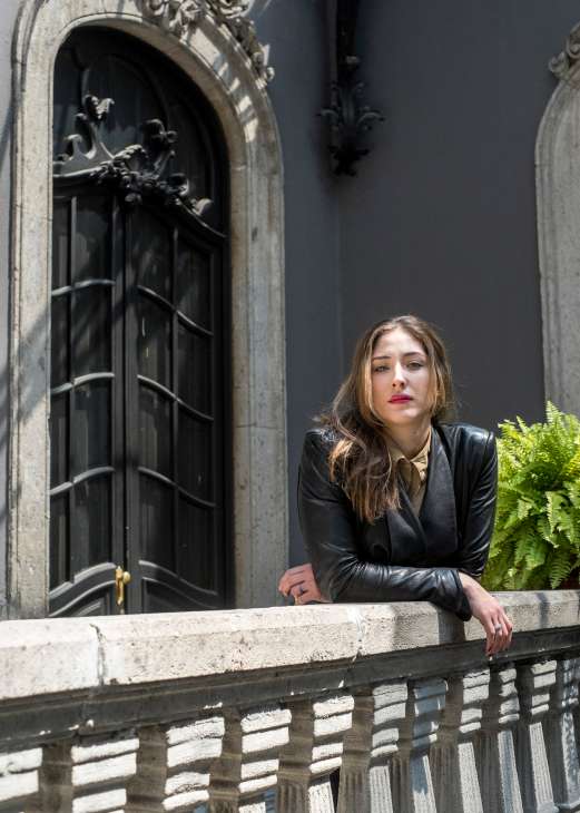 Gallerist Sofia Mariscal stands on a balcony in front of a colonial-style building with an ornate black door.