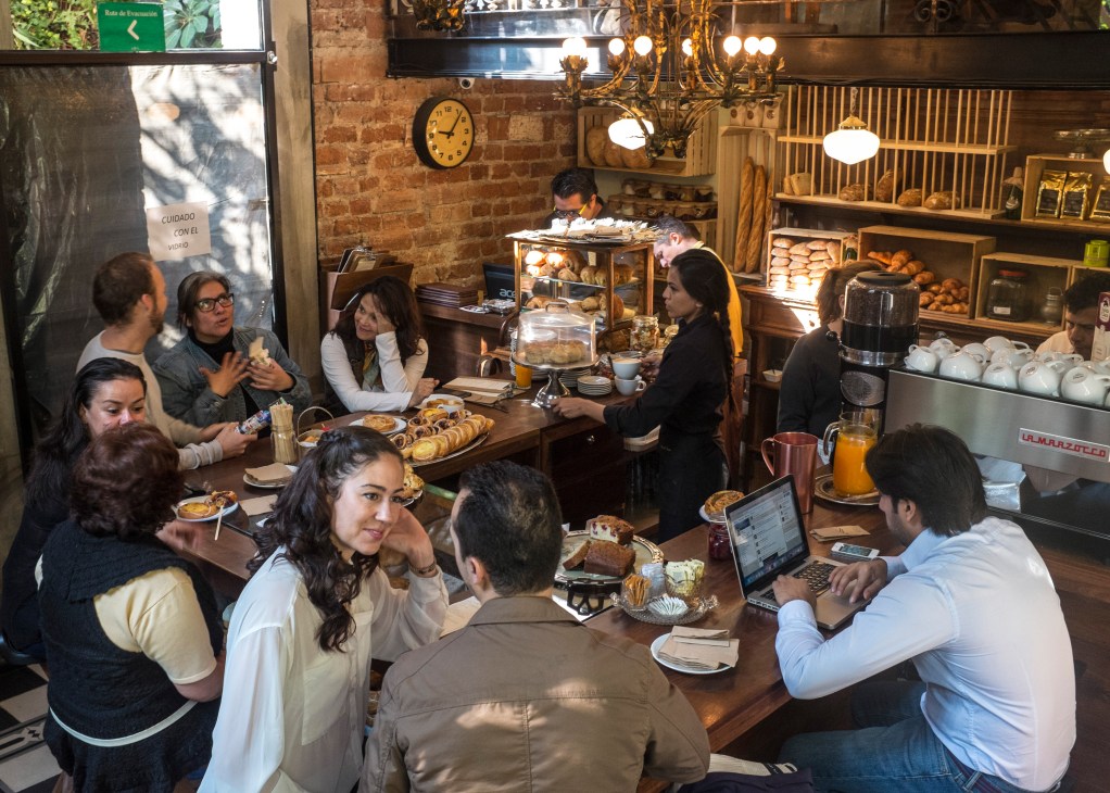 Customers eat pastries and sandwiches at wooden tables inside Panadería Havre, a Mexico City café with exposed brick walls and vintage décor.