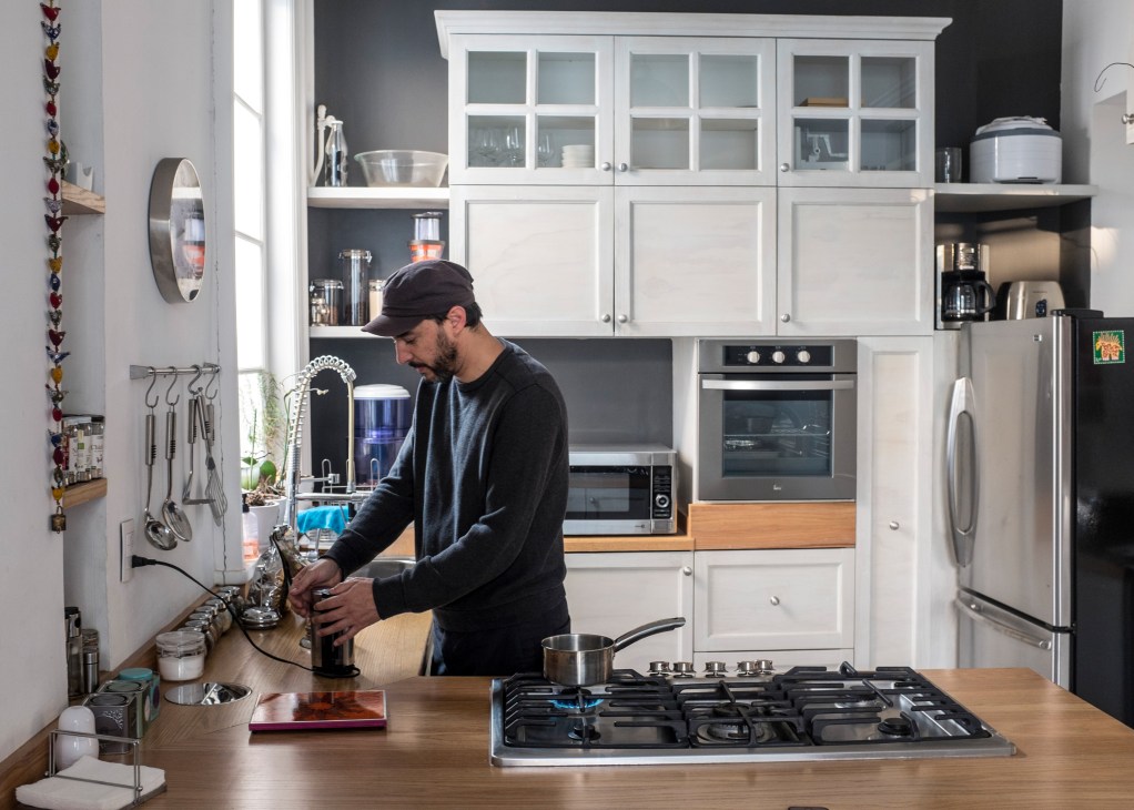 Luis San Martin stands at a kitchen counter with a gas cooktop in his modern, minimalist kitchen with white cabinetry.