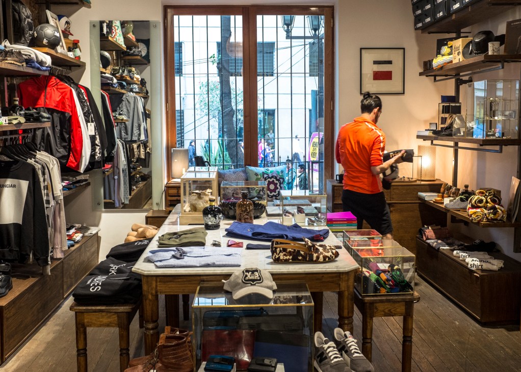 Interior of Common People Man menswear shop with clothing displays, shelving, and a person in an orange shirt at the counter.