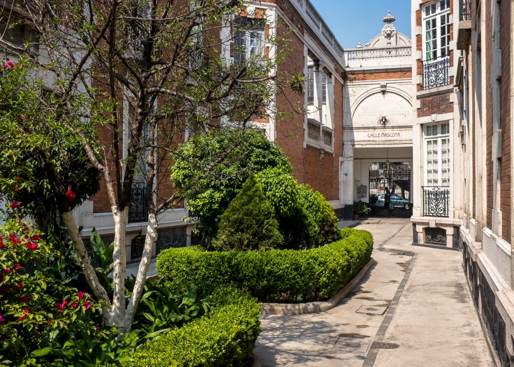 La Mascota building courtyard with manicured hedges, flowering plants, and historic brick architecture in Mexico City's Juárez neighbourhood.
