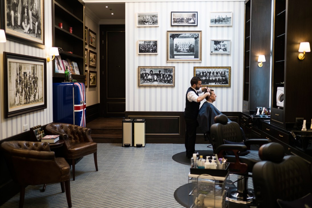A barber cuts a customer's hair at Truefitt & Hill, with vintage photographs and British memorabilia decorating the salon walls.