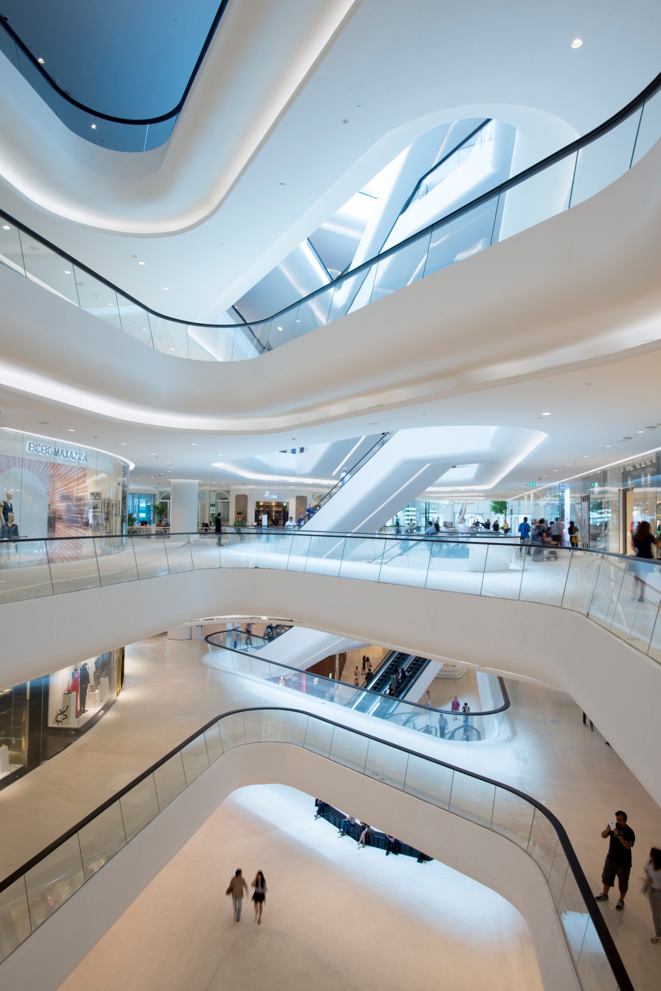 Central Embassy's main atrium with curved white balconies, escalators, and natural skylight flooding the multi-level mall interior.