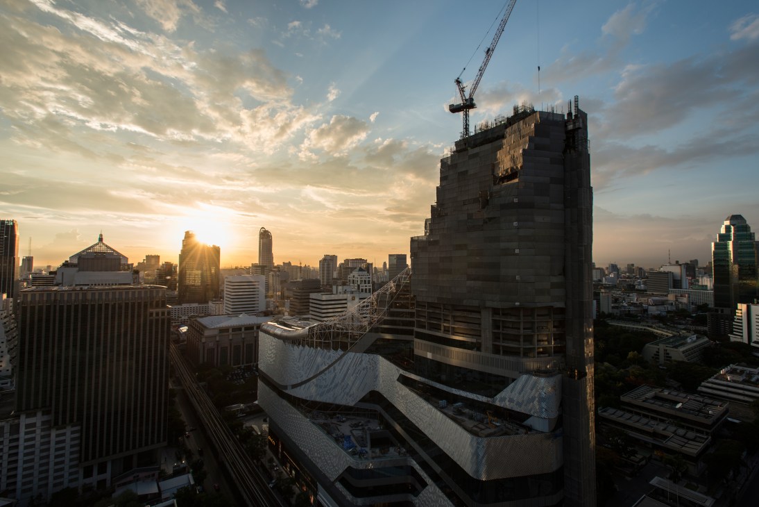 Central Embassy's curved silver facade under construction at sunset, surrounded by Bangkok's skyline.