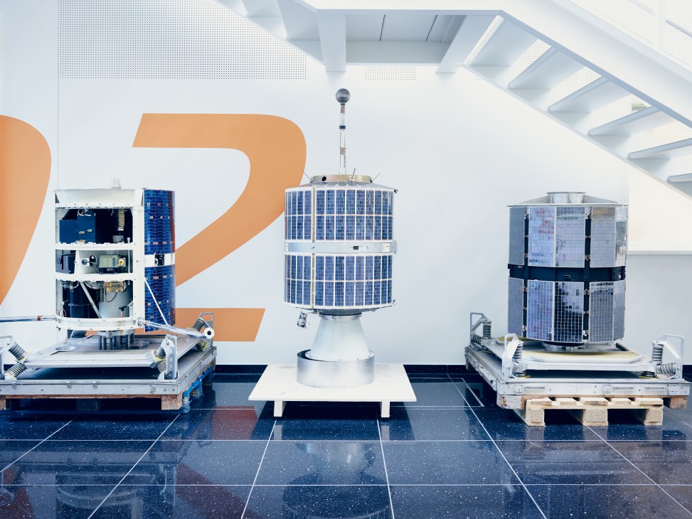 Three engineering models of European Space Research Organisation satellites displayed on a gallery floor with a large orange number 2 behind them.