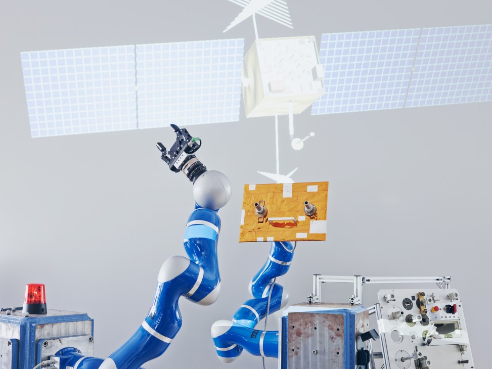 Blue and white robotic arm holding a gold panel with solar arrays and satellite model visible above.