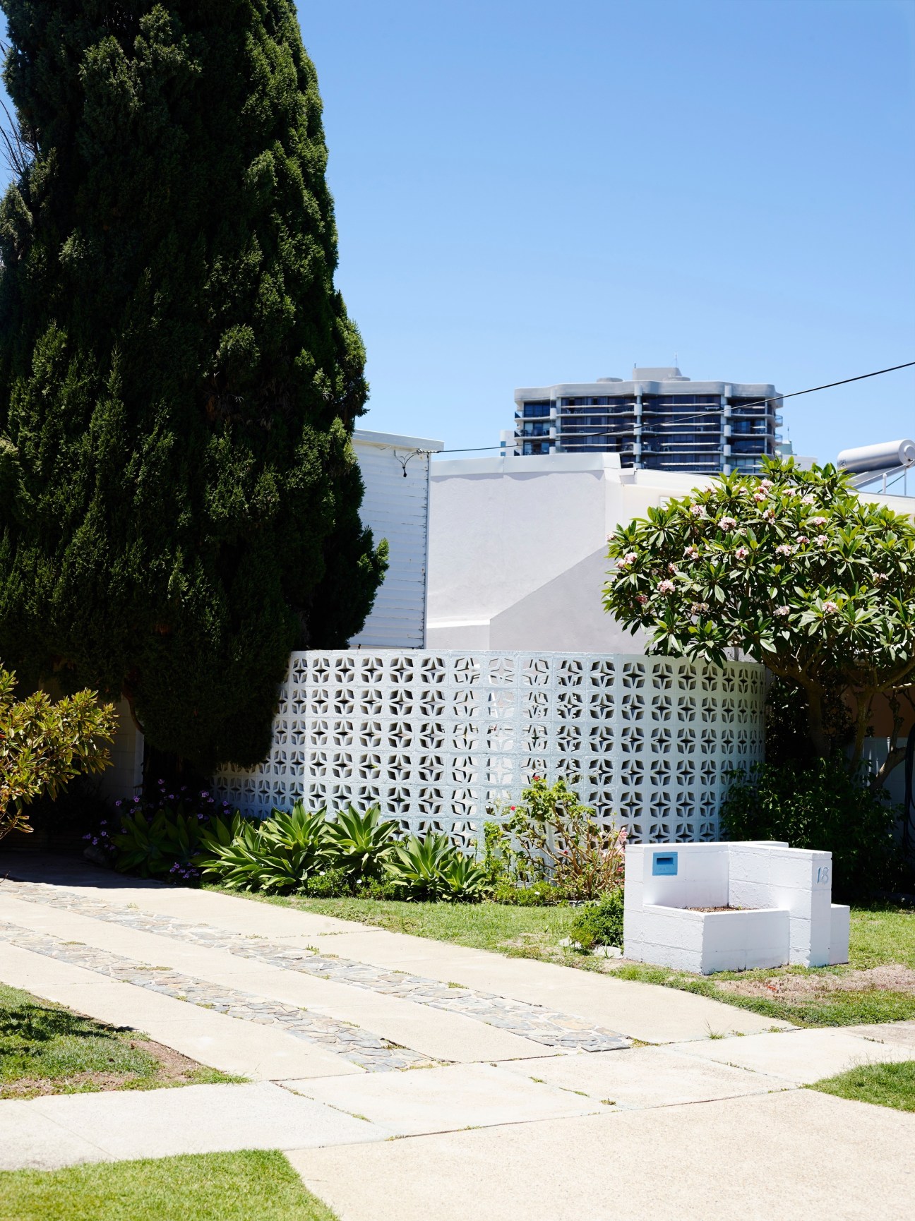 Mid-century modern white concrete screen wall with geometric pattern in front garden, backed by modern high-rise apartment building.