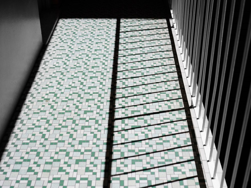 Green and white geometric tile pattern on a covered outdoor deck with shadow stripes.