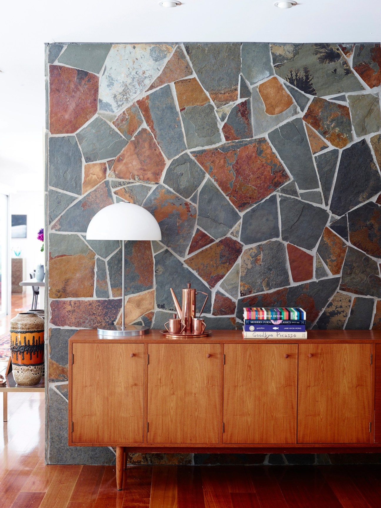 Mid-century modern interior with patterned stone wall, wooden dresser, white pendant lamp and vintage accessories.