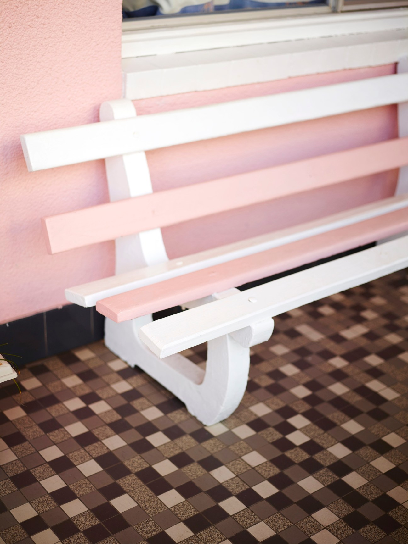 Pink wooden bench at the Coolangatta Ocean View Motel with white metal supports against checkered tile flooring.
